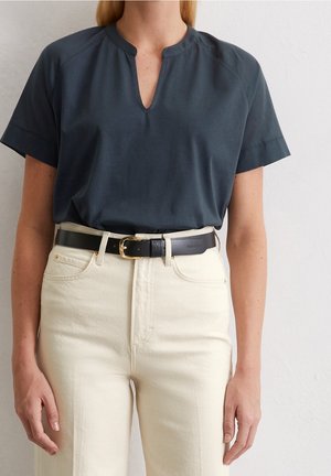 Ciemnogranatowa bluzka z dekoltem typu keyhole, krótkimi rękawami, zestawiona z kremowymi jeansami z wysokim stanem oraz czarnym paskiem ze złotą klamrą.