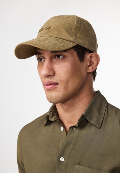 Khaki cotton cap with a pre-curved brim, embroidered "07" on the front, paired with a button-up olive green shirt.