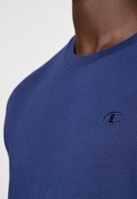 T-shirt de algodão azul-marinho com decote redondo e mangas curtas. Apresenta um pequeno logótipo bordado na área esquerda do peito. Textura suave.