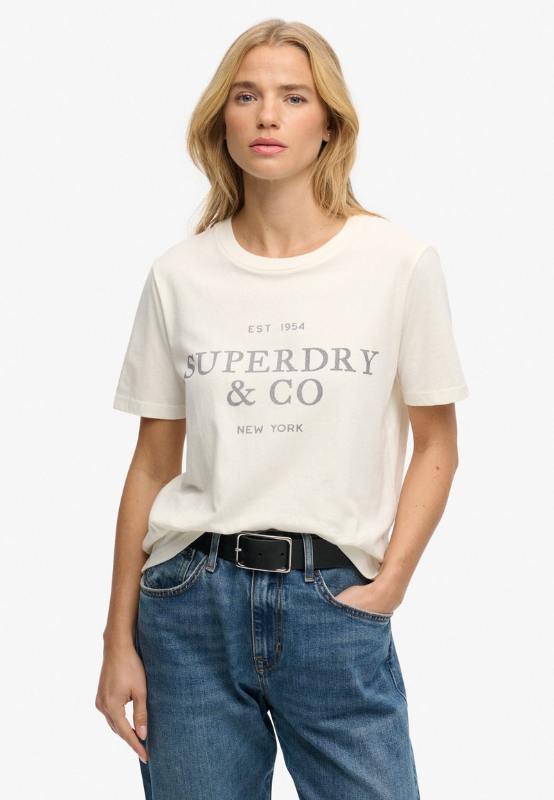Crèmekleurig katoenen T-shirt met de opdruk "SUPERDRY & CO NEW YORK" in donkergrijs. Korte mouwen, ronde hals, losse pasvorm.