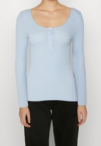 Light blue long-sleeve top made of ribbed material featuring a scoop neckline and three button accents at the front.