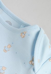 Hele sinine puuvillane beebikombinesoon, millel korduv karupilt beeži ja siniste triipudega, pehme soonikkoe kaelusega ja õmmeldud servadega.