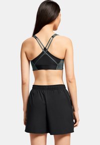 Sujetador deportivo negro con tirantes cruzados y detalles en verde, combinado con pantalones cortos negros de cintura elástica. Textura suave y diseño ajustado.
