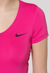 Fitted, short-sleeve athletic top in bright pink fabric, featuring a black Nike swoosh logo on the left side. Scoop neckline design.