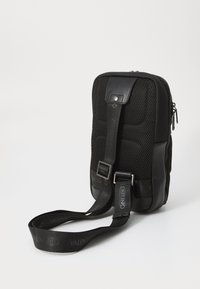 Borsa a tracolla in rete nera e pelle con chiusura a zip, tracolla regolabile e dettagli del marchio sulla tracolla. Forma rettangolare con texture imbottita.