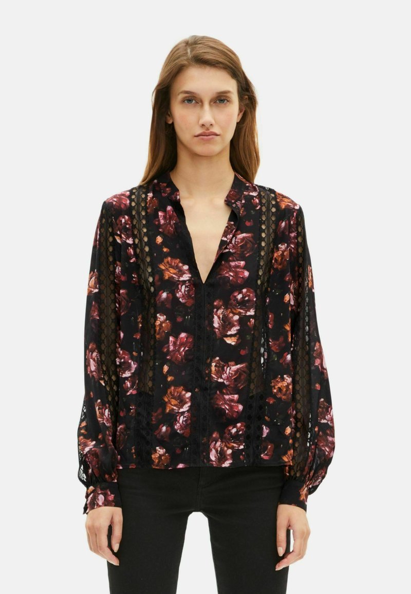 Blusa nera con stampa floreale nei toni del rosso e dell'arancione. Tessuto trasparente con dettagli in pizzo, maniche lunghe e scollatura a V profonda.