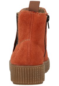 Oranssi mokkanahkasaapas nilkkapituisella ruskealla kumipohjalla, jossa on sivuvetoketju ja kangasviimeistely helppoa käyttämistä varten. Sujuva pinta ja ompeleiden yksityiskohdat.