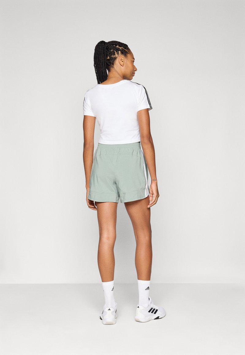 T-shirt blanc court avec des rayures noires, associé à un short de sport vert menthe. Le mannequin porte des chaussettes blanches et des chaussures de sport accentuées de noir.
