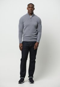 Grau zipfelpullover aus Wollmischung, kombiniert mit dunklen Jeans und dunklen Sneakern. Schlichtes Design, taillierte Silhouette, glatte Textur.
