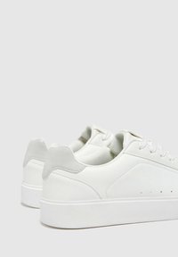 Białe sneakersy wykonane z gładkiej skóry, z płaską podeszwą, okrągłym noskiem i minimalistycznym designem z jasnoszarymi akcentami oraz perforowanymi detalami.