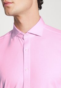 Rosa polo skjorte med en klassisk krave, korte ærmer og en stolpe med lyse knapper. Glat, let stofstruktur.
