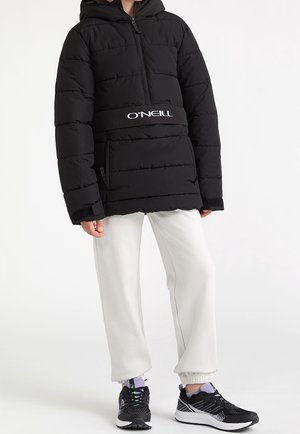 Doudoune noire avec fermeture éclair sur le devant et capuche, dotée d'une large ceinture logo O'Neill. Associée à un pantalon de survêtement gris clair et des baskets noires.