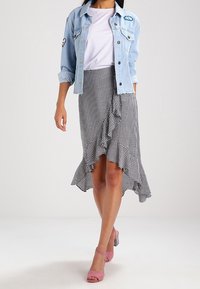 Veste en denim, bleu clair, avec des patches en forme de nuage et de cœur ; t-shirt blanc ; jupe vichy noir et blanc avec ourlet en volants ; sandales à talons roses.