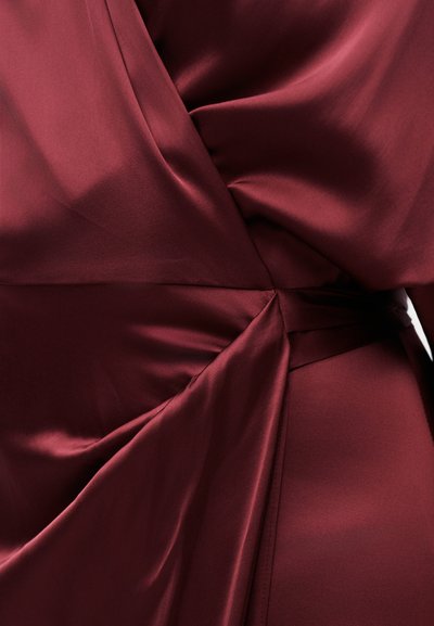 Υφασμα σατέν σε βαθύ μπορντό με ρυθμίσεις και μαζέματα στη μέση, δημιουργώντας απαλές πτυχώσεις και εφέ τύλιγματος.