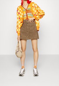 Cardigan lavorato a maglia colorato con motivi a scacchi e cuori, indossato su una maglietta a righe, abbinato a una gonna in velluto a coste e scarpe sportive.