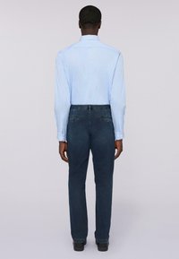 Camisa de manga larga a rayas en azul claro y blanco con puños abotonados, combinada con pantalones vaqueros oscuros de pierna recta. Tela suave, ajuste entallado.