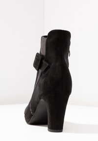 Zwarte enkellaars van suède met een hoge hak, voorzien van een textuur mesh paneel en een zijrits, geaccentueerd met een klein decoratief riempje.