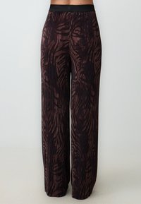 Schwarze weit geschnittene Hosen mit braunem Zebra-Streifenmuster, aus strukturiertem Stoff mit glattem Bund. Vertikale Rippdetails.