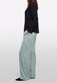 Svart långärmad topp i kombination med ljus mintfärgade vida byxor med en subtil textur, kompletterat med spetsiga svarta skor.