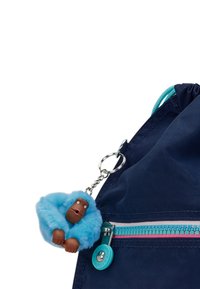 Marineblå stof rygsæk har en turkis lynlås, rosa detaljer og en fluffy blå abe nøglering med et brunt ansigt og åben mund.