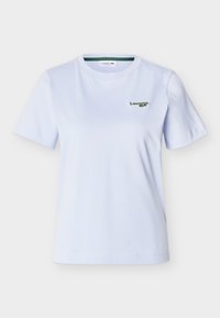 T-shirt blanc à manches courtes avec col rond et petit logo vert Lacoste sur le côté gauche de la poitrine, sur fond uni.