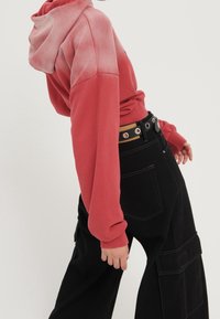 Felpa rossa sfumata con maniche lunghe e cappuccio, abbinata a pantaloni neri oversize con tasche e cintura a più fori.