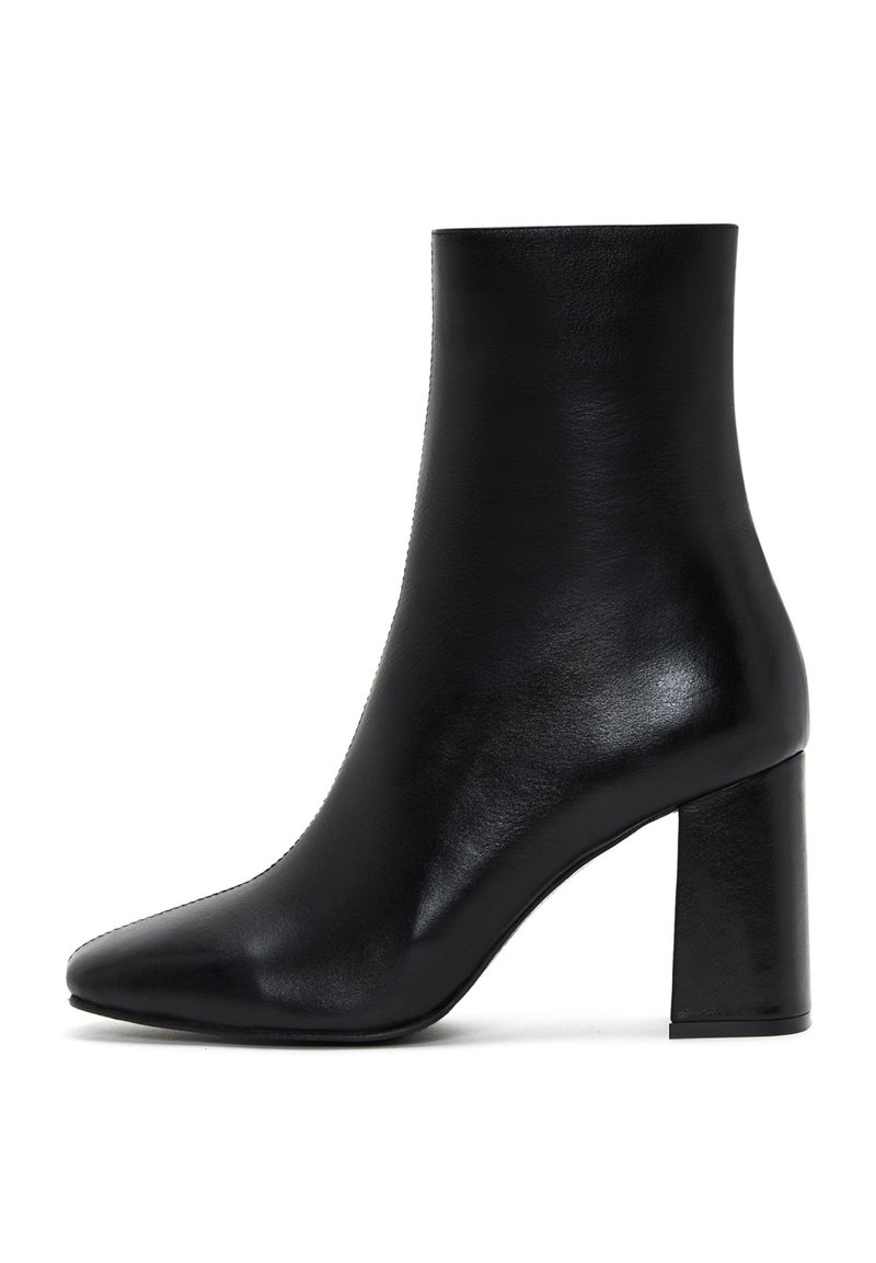 Bottine en cuir noir avec un bout pointu, une texture lisse et un talon large, présentant un design épuré et minimaliste.