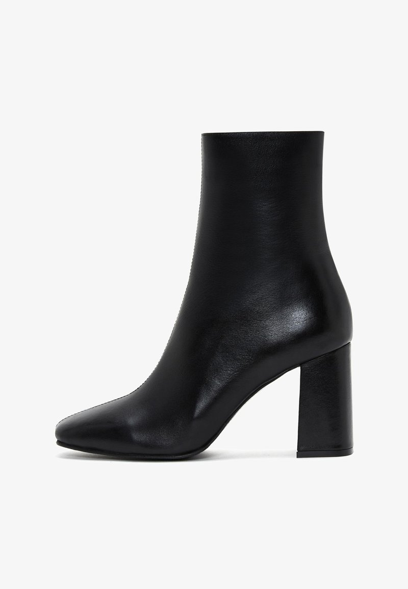 Bottine en cuir noir avec un bout pointu, une texture lisse et un talon large, présentant un design épuré et minimaliste.