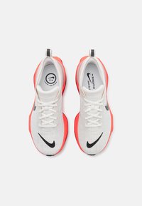 Nike ZoomX sportcipők, fehér hálós felsőrész, piros gumitalp, fekete swoosh logó és fehér fűzők jellemzik. Könnyű kényelmet nyújtó kialakítás.