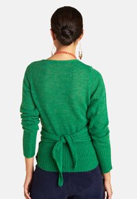 Green knitted sweater with a tie at the waist, ribbed cuffs, and relaxed fit. Soft texture and mid-weight material.