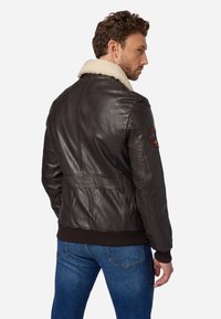 Braune Lederjacke mit einem cremefarbenen Schafsfellkragen, gerippten Bündchen und einem detaillierten Schulterpatch; taillierte Passform mit glatter Textur und Rückennähten.