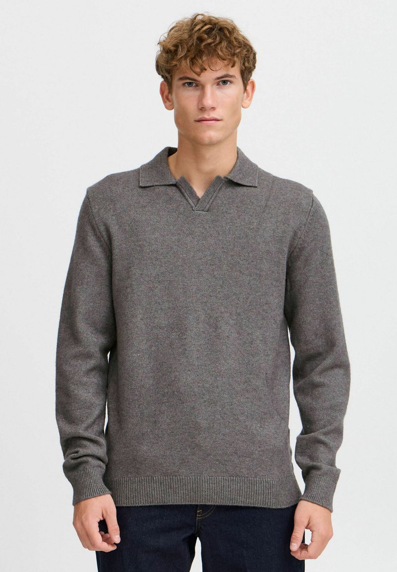 Grauer Strickpullover mit V-Ausschnitt und Kragen. Lange Ärmel und gerippter Saum. Weicher Stoff, schlichtes Design. Über dunklen Jeans getragen.
