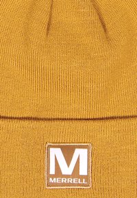 Bonnet en tricot moutarde avec une texture côtelée et un revers replié ; présente une étiquette carrée de logo Merrell en blanc et or à l'avant.