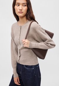 Μπεζ πλεκτή ζακέτα με στρογγυλή λαιμόκοψη, κλείσιμο με κουμπιά και μακριά μανίκια. Συνδυάζεται με σκούρα τζιν και καφέ τσάντα ώμου.