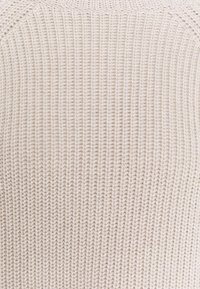 Pull beige clair en maille avec une texture côtelée et des manches raglan, fabriqué dans un matériau doux et confortable avec un col sans couture.