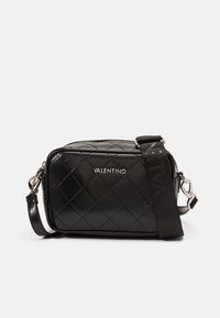 Černá prošívaná kožená crossbody taška se stříbrným kováním a odnímatelným popruhem, s uzavíráním na zip a reliéfním logem na přední straně.