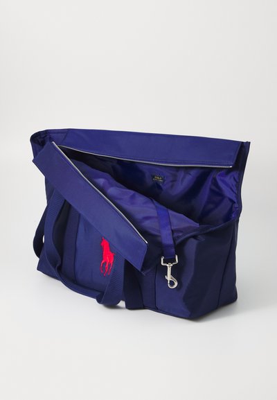 Navy nylon bag with a red embroidered logo, zip closure, adjustable strap, and dual handles. Interior features a smooth, lined finish.