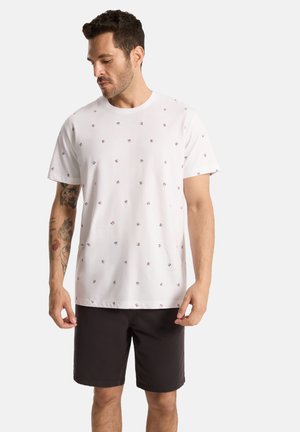 Biała bawełniana koszulka z rozproszonym wzorem czerwonych i niebieskich linii. Połączona z ciemnymi szortami, prezentując luźny krój i krótkie rękawy.