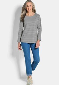 Graues gestreiftes langärmliges Hemd mit einem runden Halsausschnitt, kombiniert mit hellblauen Jeans und beigen Sneakers, mit hochgekrempelten Ärmeln.