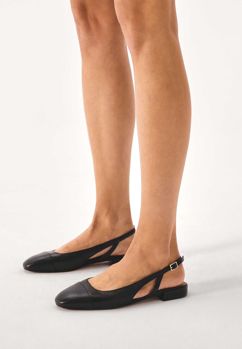 Black leather slingback flats with a pointed toe, cut-out design, and a small gold buckle accent at the heel. Smooth texture and minimalist style.