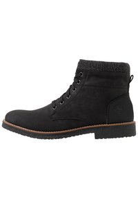 Bottines noires montrées avec un extérieur lisse, un haut en tricot gris, un bout rond, cinq œillets en métal et une semelle en caoutchouc texturé avec un contour marron.