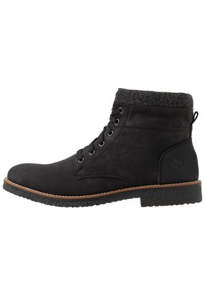 Botas negras hasta el tobillo con un exterior liso, puño de punto gris, puntera redonda, cinco ojales de metal y una suela de goma texturizada con un borde marrón.