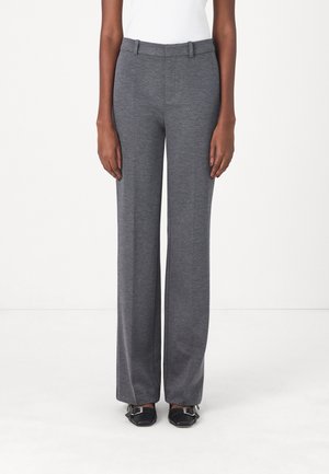 Pantalon gris à larges jambes fabriqué en tissu doux, avec une texture lisse, des passants de ceinture et une coupe ajustée, associé à des chaussures noires.