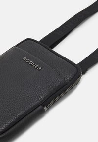 Borsa in pelle nera con superficie testurizzata, dotata di chiusura con zip e tracolla. La parte anteriore presenta un logo "BOGNER" in rilievo.