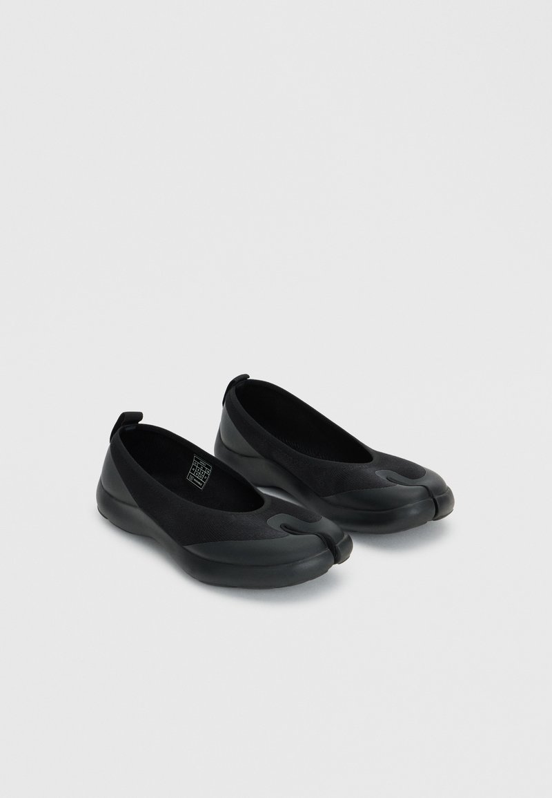 Pair of black slip-on shoes with split-toe design and rubber soles on a light gray background.