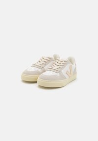 Sneaker beige e bianche con tomaia in suede e rete testurizzati, caratterizzate da un logo con accento rosa, design con lacci e suola in gomma beige chiaro.