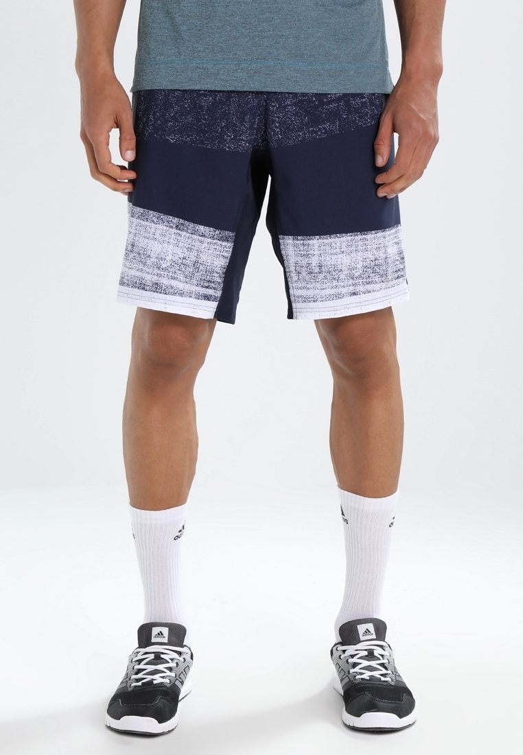 Shorts de sport bleus marine et blancs avec un motif texturé, assortis à des chaussettes de sport blanches et des chaussures de course noires.