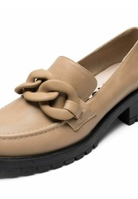 Mocassino in pelle beige con una prominente catena beige sul davanti, suola in gomma nera testurizzata e cuciture lungo la parte superiore.