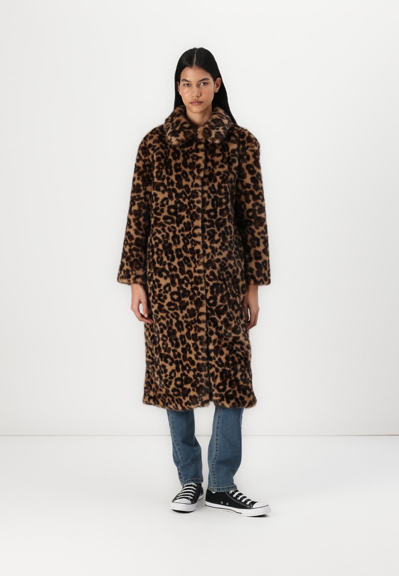 Palton din blană sintetică cu imprimeu de leopard, guler înalt, mâneci lungi și o siluetă dreaptă, asortat cu blugi bleumarin și adidași negri.