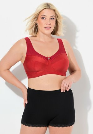 Reggiseno rosso texture con spalline larghe e un fiocco decorativo al centro, abbinato a pantaloni corti neri con rifiniture in pizzo. Design semplice, senza fantasie.